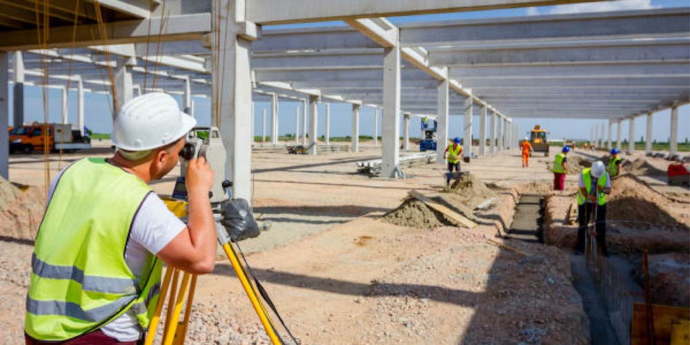 Man in hard hat and vest surveys a construction site with workers and equipment